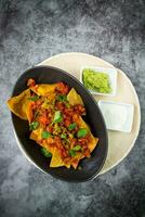 nachos with sauce, meat and herbs in a black plate, top view photo