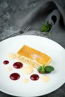 white sponge cake with drops of syrup, mint and wild berries on a round plate side veiw photo