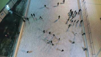 People are skating on illuminated ice rink in the evening. Aerial vertical top-down view. Establishing shot. Drone is flying forward. video