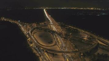 beleuchtet Komplex Autobahn Kreuzung und Autos der Verkehr Marmelade beim Winter Nacht. Drohne ist fliegend nach vorne, Kamera ist kippen runter. Antenne Sicht. Festlegung Schuss. video