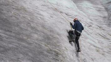 alpinista uomo nel ramponi è utilizzando jumar su fisso corda per Ascend su ripido nevoso pendenza nel montagne. lento movimento video