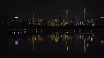 Manhattan Urbain paysage urbain et réflexion dans jacqueline Kennedy onassis réservoir dans central parc à nuit. Nouveau york ville. uni États de Amérique. panoramique coup video