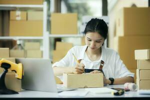 Online business owner writing customer address on a parcel box before shipping photo