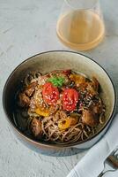 noodles with beef, vegetables, cherry tomatoes and sesame sauce in a deep plate side view photo