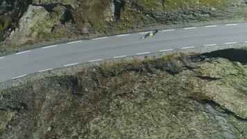 ciclistas en cascos son carreras en montaña la carretera en Noruega a soleado verano día. aéreo vertical De arriba hacia abajo vista. zumbido es volador oblicuo video