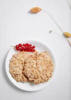 whole grain cookies with a sprig of red currants in a small white plate top view photo