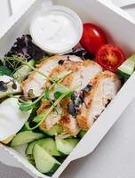 pieces of chicken with vegetables, herbs and sauce in a lunchbox photo