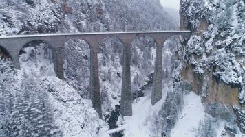 terraplén viaducto con ferrocarril a invierno Nevado día en Suiza. aéreo vista. suizo Alpes. nevando zumbido moscas adelante y hacia arriba video