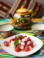 caprese salad with mazzarella tomatoes and herbs in oriental style on a table with a teapot and a cup for tea. photo