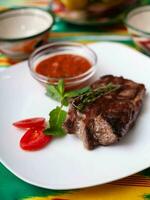 beef steak with tomato sauce, tomatoes and herbs in oriental style on a table with a teapot and a cup for tea. photo