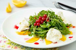 green salad with arugula and lingonberries on a white plate and marble background top view photo