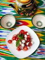 caprese ensalada con mazarella Tomates y hierbas en oriental estilo en un mesa con un tetera y un taza para té. foto