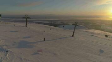 People are Skiing and Snowboarding on Ski Slope with Cable Car at Sunny Winter Sunset. Aerial View. Drone is Flying Sideways. Establishing Shot.. video