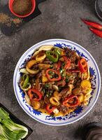 noodles with bell pepper, potatoes, meat and herbs in a plate with a pattern top view photo