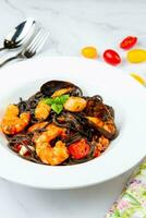 black noodles with mussels, shrimp, tomatoes and herbs side view photo