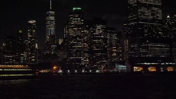 Manhattan urbano Horizonte às noite e enviar. Novo Iorque cidade. Visão a partir de a água. Câmera inclina acima video