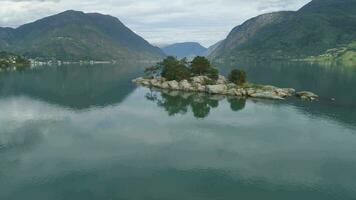 Basso livello volante al di sopra di isola nel fiordo con verde montagne su sfondo. lustrafiordo, Norvegia. riflessione nel acqua. aereo Visualizza. fuco è volante inoltrare e ascendente video