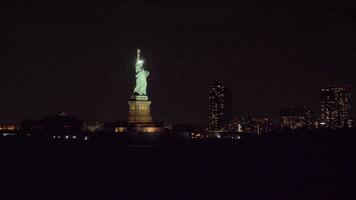 upplyst staty av frihet på natt och byggnader av ny york stad. se från de vatten. kretsande video