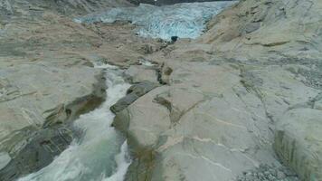 låg nivå flygande över stenar och vatten ström mot smältande Nigardsbreen glaciär i Norge. antenn se video