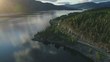 fliegend Über Straße mit Autos und kroderen See Ufer im Norwegen beim Sonnenuntergang. Antenne verraten Schuss. Grün Berg mit Bäume. Drohne ist fliegend nach vorne, Kamera ist kippen oben video