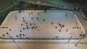 People are skating on ice rink in the sunny day. Aerial vertical top-down view. Establishing shot. Drone is flying sideways video