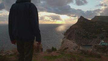 Silhouette of man in jacket and cap walking to the edge of rocky cliff video
