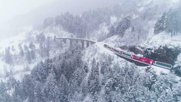 GRAUBUNDEN, SWITZERLAND - FEBRUARY 11, 2019 Viaduct and Glacier Express Train in Winter Day. Snowing. Swiss Alps. Switzerland. Aerial View. Drone Follows Train video