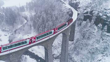 GRAUBUNDEN, SWITZERLAND - FEBRUARY 11, 2019 Landwasser Viaduct and Glacier Express Train in Winter Day. Snowing. Swiss Alps. Switzerland. Aerial View. Drone Flies Forward, Camera Tilts Up video