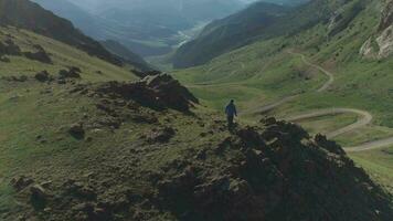 promeneur homme des stands sur Haut de Montagne de pointe plus de serpentin route passer dans ensoleillé été journée. drone est en orbite autour. aérien voir. établissement tir. Kirghizistan video