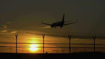 silhueta do avião aterrissagem às a aeroporto às ensolarado pôr do sol contra a Sol. lento movimento video