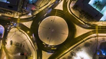 beleuchtet der Verkehr Kreis im das Stadt und Autos beim Winter Nacht. runden Kreuzung. Antenne Vertikale von oben nach unten Sicht. hyper Ablauf. Drohne fliegt nach oben und dreht sich video