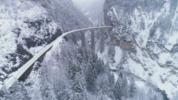 landwasser viadukt med järnväg på vinter- snöig dag i schweiz. antenn se. swiss alperna. snöar. Drönare flugor fram, kamera lutar upp video