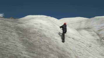 alpinista uomo nel ramponi e casco è utilizzando bloccante su fisso corda su montagna pendenza a soleggiato giorno. lento movimento video