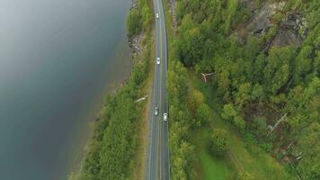 carros son yendo en país la carretera cerca lago en Noruega en verano nublado día. aéreo revelar vista. zumbido es volador adelante, cámara se inclina arriba video