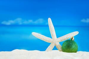 Shiny green ball with starfish on sand of beach. Christmas, New Year. Copy space photo