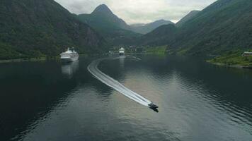 klein motor snelheid boot en groot reis voering in geiranger fjord in zomer dag. Noorwegen. antenne visie. dar is vliegend achteruit, camera is kantelen naar beneden video