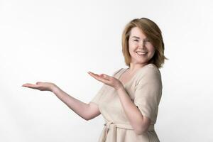 Portrait of female in beige dress looking at camera, standing on white background, with palms up photo