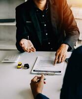 A car rental company employee is handing out the car keys to the renter after discussing the rental details and conditions together with the renter signing a car rental agreement. Concept car rental. photo