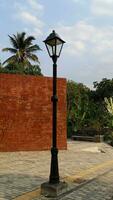 garden lamppost against the background of red brick wall, trees, clear sky photo