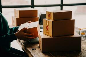 Emprendedora de pequeñas empresas o mujer asiática independiente que usa una computadora portátil con caja, joven mujer asiática de éxito con su mano levantada, caja de embalaje de marketing en línea y entrega, concepto de pyme. foto