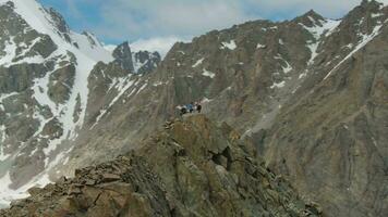 Four Climbers on Peak of Rock. Snow-Capped Mountains. Aerial View. Drone is Orbiting video