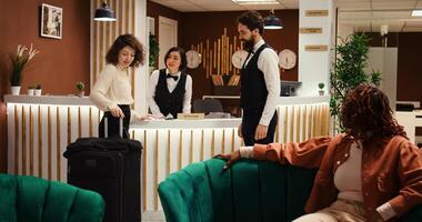 Tourist on vacation ringing concierge bell at reception desk in stylish hotel lobby, being helped by bellboy and receptionist. Helpful resort staff assisiting happy guest with room booking check in photo