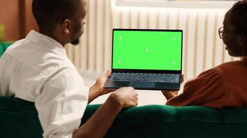 Bored tourists watching video on laptop chroma key green screen mock up waiting for check in process to be over. Guests sitting in hotel foyer while porter employee carries luggage to their room photo