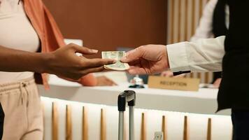 Close up of thankful hotel guest tipping helpful bellboy after receiving great customer service. African american woman handing dollar banknote to porter employee for helping with baggage photo