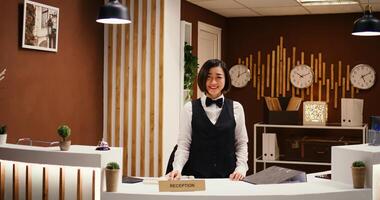 Happy professional asian hotel employee taking phone calls while working at reception counter. Joyful smiling receptionist taking travel accommodation booking requests standing at check in front desk photo