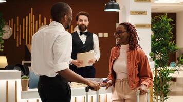 African american couple checking out from luxury hotel after successful honeymoon vacation. Happy guests assisted by friendly helpful front desk receptionist in resort lobby photo