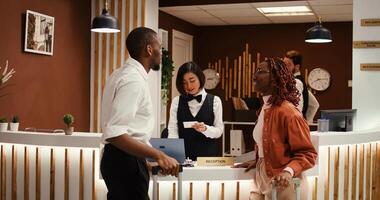 Cheerful relaxed guests leaving hotel after nice stay, checking out. Tourists handing over room access card key to friendly professional concierge personnel at reception desk photo