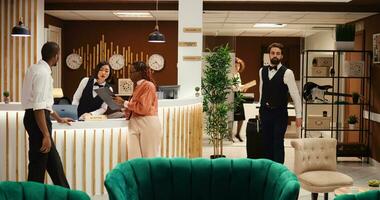 Tourists filling in personal information in order to be checked in their room, helped by friendly asian receptionist. Busy hotel staff performing tasks in hotel foyer while guests are being booked in photo