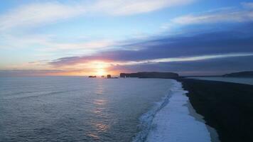 Arctic reynisfjara black sand beach on spectacular nordic landscape with sunset and ocean waves crashing on shore. Aerial view of icelandic coastline and natural scenery. Slow motion. photo