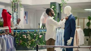 Meticulous retail assistant working in luxury fashion boutique, arranging pocket square on blazer. Experienced african american employee showcasing new collection of trendy garments on mannequin video